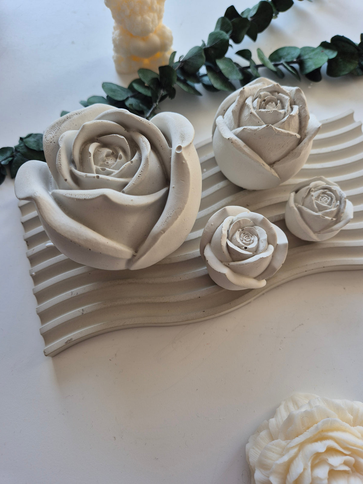 Betonrosen in mehreren Größen auf einem gewellten Tablett, daneben ein Eukalyptuszweig