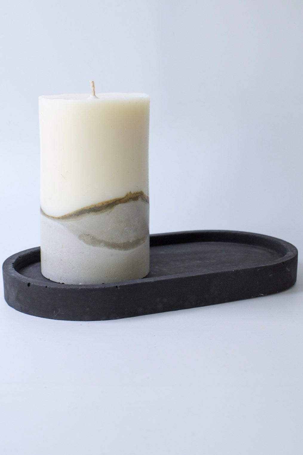 Olivenwachskerze mit Betonsockel von der Seite auf einem schwarzen Tablett